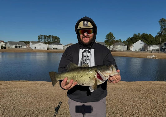 Angler fishing from the bank of a calm river with scenic surroundings, demonstrating ideal travel fishing setup.